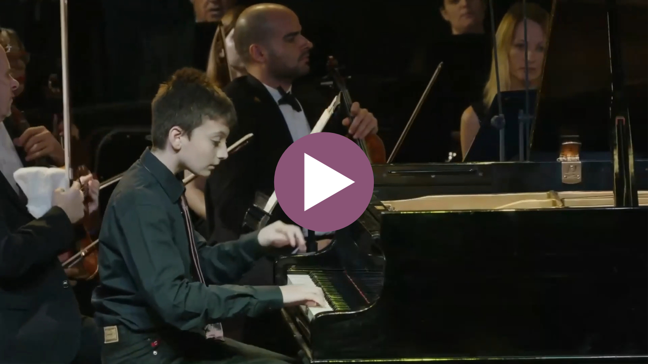Musiah piano student, Ariel Waldman, seated at a grand piano playing Beethoven's Piano Concerto No. 1 with full orchestra. Click to play the video.